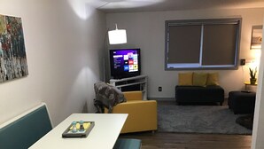 Kompakti olohuone, jossa on ruokapöytä, sohva, televisio ja pieni ikkuna.
