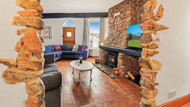 A cozy living room with a stone fireplace, a blue sofa, and a television mounted on the wall. - Victorian style home, where shabby chic meets the beach (Torquay)