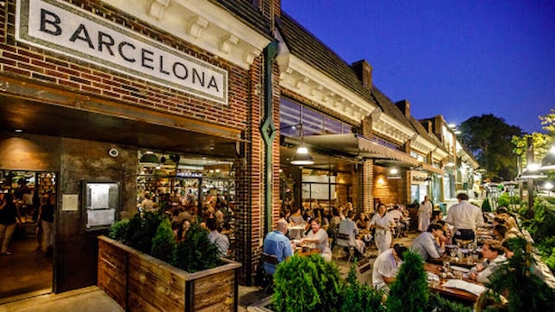 A bustling outdoor dining area with a brick facade and a sign reading "BARCELONA".