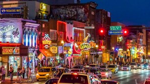 A busy urban street at night with various illuminated signs and storefronts.
