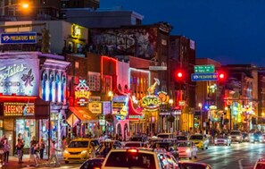 Une rue animée d’une ville, de nuit, avec de nombreuses enseignes et vitrines illuminées.