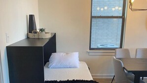 Een kleine kamer met een bed, een tafeltje en een raam met jaloezieën.