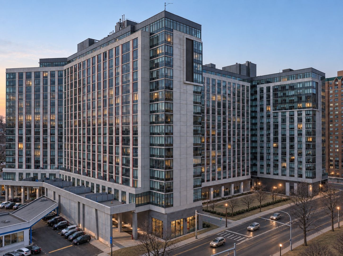 A multi-story hotel with a modern architectural design, featuring a large parking area and a well-lit entrance.