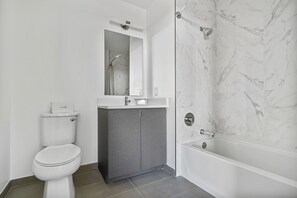 A modern bathroom with a toilet, vanity, mirror, and a bathtub with a showerhead. - Global Luxury Suites White Plains (White Plains)