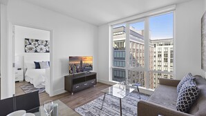 Una sala de estar moderna con una mesa de centro de vidrio, un sofá, un televisor y un amplio ventanal con vistas a la ciudad.