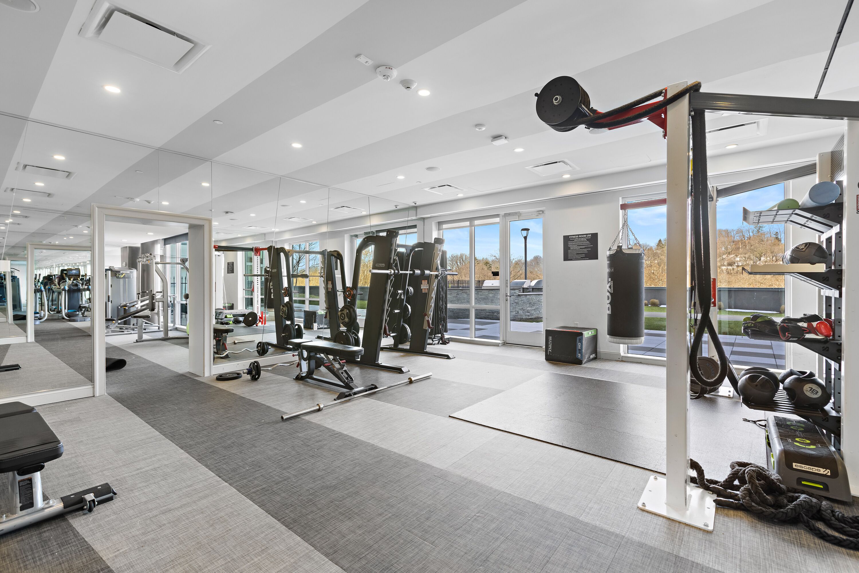 A modern gym with various exercise equipment, large windows, and a clean, spacious layout.