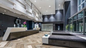 Un área de recepción moderna con suelo de madera en espiga, una mesa de recepción, zona de estar y ventanas amplias.