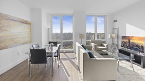 Una sala de estar moderna con comedor, ventanas amplias, televisor de pantalla plana y vista a la ciudad.