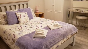 A neatly made bed with floral bedding, a bedside table with a lamp, and a small stool. - # 5 Central Killarney Apartment (KILLARNEY)
