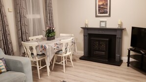 A living room with a fireplace, a television, a dining table with chairs, and a sofa. - # 5 Central Killarney Apartment (KILLARNEY)