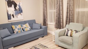 A living room with a grey sofa, a light blue armchair, and a patterned rug. - # 5 Central Killarney Apartment (KILLARNEY)