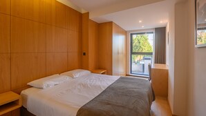 Une chambre d’hôtel moderne avec un grand lit, des panneaux de bois au mur, une petite table de chevet et une vue sur l’extérieur grâce à une grande fenêtre.