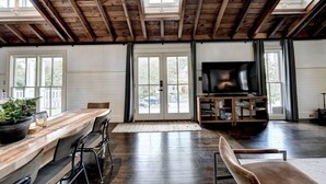 Ein großzügiger Wohnbereich mit Holzboden, einem großen Fernseher und einem Essbereich mit einem Holztisch und Stühlen.