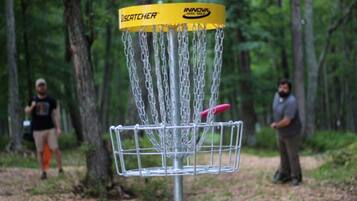 Ein Discgolf-Korb mit Ketten und einem gelben Aufleger mit dem Schriftzug 'INNOVA' in bewaldeter Landschaft.
