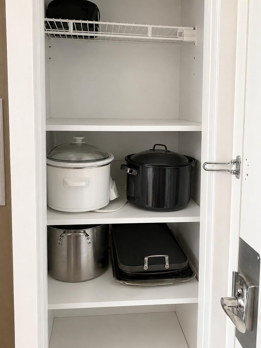 A white pantry with shelves containing pots and a kettle.