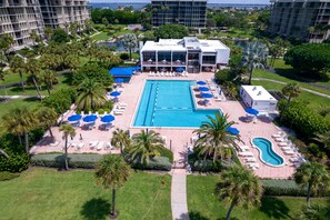 Relax by the large pool surrounded by sun loungers and umbrellas, with a serene lawn and trees nearby.