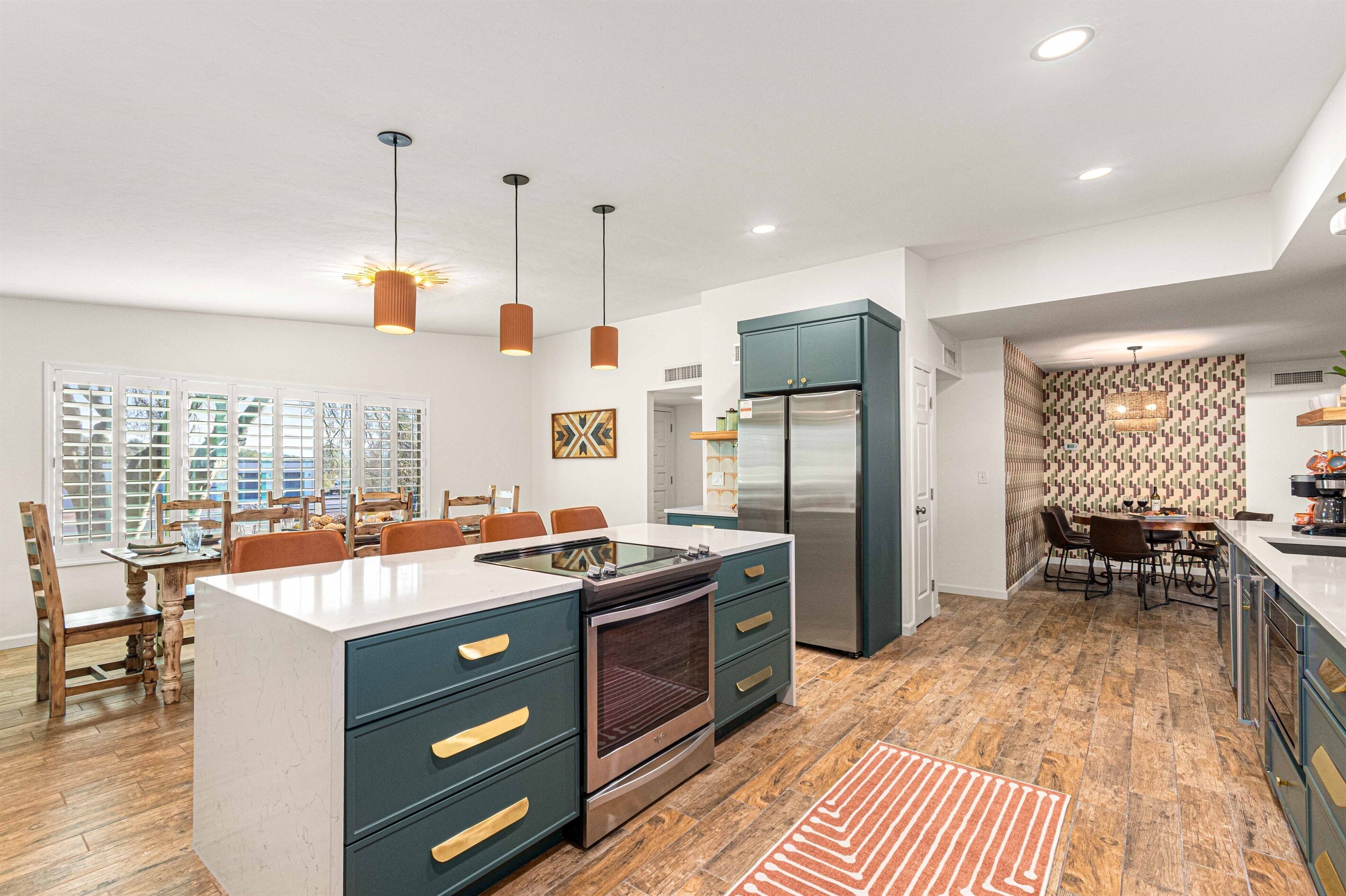 A modern kitchen with a central island, built-in appliances, pendant lighting, and a dining area with wooden chairs.