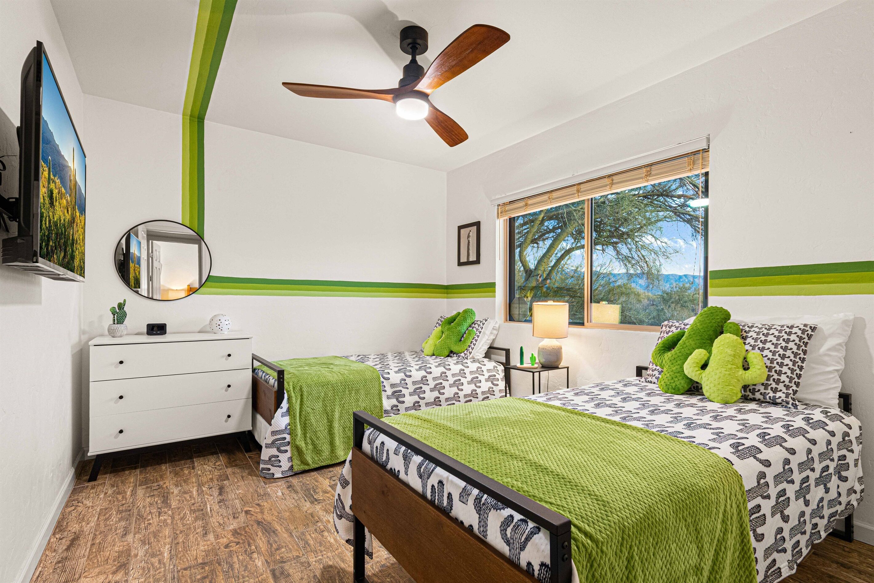 Une chambre avec deux lits, un ventilateur de plafond, une fenêtre avec vue, une commode et un miroir.