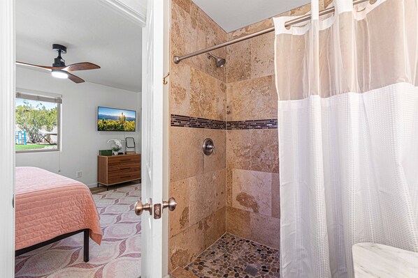 Une salle de bain équipée d’une douche, de toilettes, d’un lavabo et d’une fenêtre donnant sur les arbres.