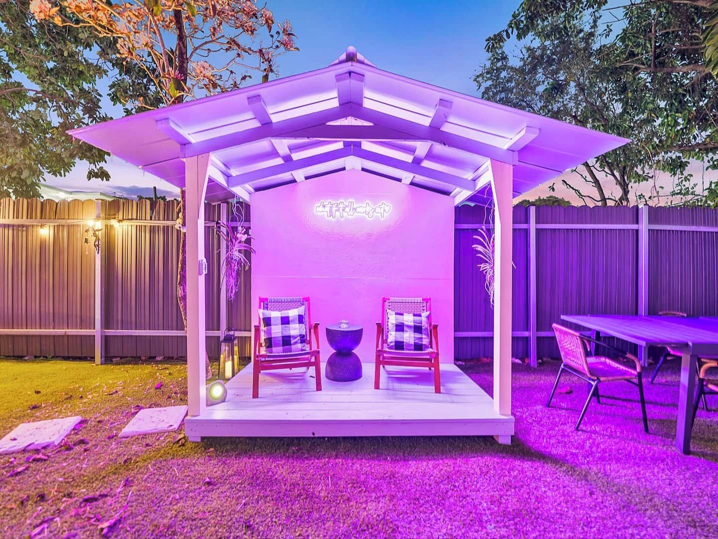 Un espace extérieur abrité, aménagé avec deux chaises et une table, et entouré d’une clôture en bois.