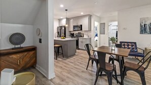 Une cuisine moderne avec des meubles blancs, un îlot central et un coin repas comprenant une table et des chaises en bois.