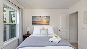 Une chambre à coucher avec un lit, une table de chevet, une lampe, un tableau et une porte.