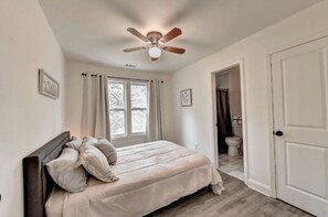 Cozy retreat with a large bed, headboard, and multiple pillows, featuring a ceiling fan and a door to a bathroom with a toilet and shower area.