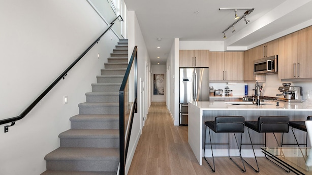A modern kitchen with a central island, stainless steel appliances, and a staircase with glass railings. - Luxurious, Ocean View 2 Story Penthouse - Downtown - Secure Parking (Victoria)