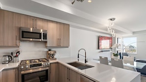 A modern kitchen with stainless steel appliances, wooden cabinets, and a central island with a sink. - Luxurious, Ocean View 2 Story Penthouse - Downtown - Secure Parking (Victoria)