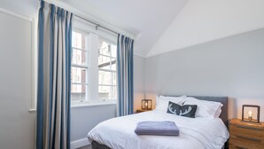 A bedroom with a bed, bedside table, and a window with curtains. - Superbly located St Andrews 2 bedroom apartment.  Beach and golf close by! (St Andrews)