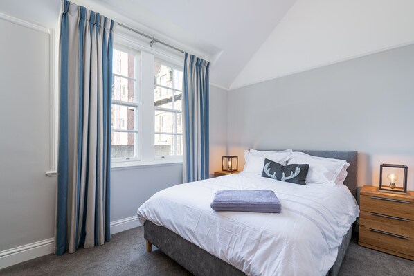 A bedroom with a bed, bedside table, and a window with curtains.