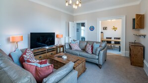 A living room with a television, sofa, coffee table, and a chandelier. - Superbly located St Andrews 2 bedroom apartment.  Beach and golf close by! (St Andrews)
