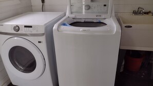 Un espace buanderie comprenant un lave-linge à chargement frontal et un sèche-linge, une fenêtre avec une prise de courant et un évier avec un robinet.