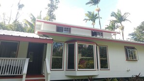 Une maison à deux étages, à l’extérieur rouge et blanc, avec de grandes fenêtres et un porche doté d’une balustrade blanche.