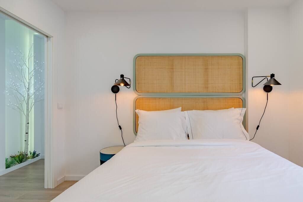 A modern bedroom with a large bed, two bedside lamps, and a view of a tree through a glass door.