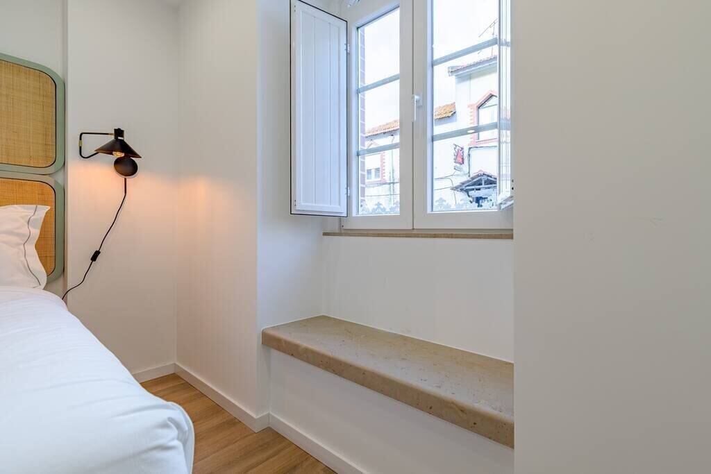 Une chambre à coucher avec un lit, une lampe de chevet, une fenêtre et un petit banc.