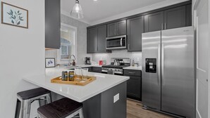 A modern kitchen with grey cabinets, a stainless steel refrigerator, a microwave, and a wooden island with stools.