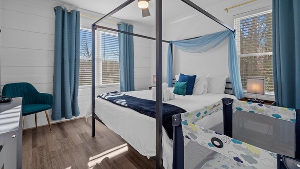 A four-poster bed with a canopy, a desk with a chair, and a window with curtains.