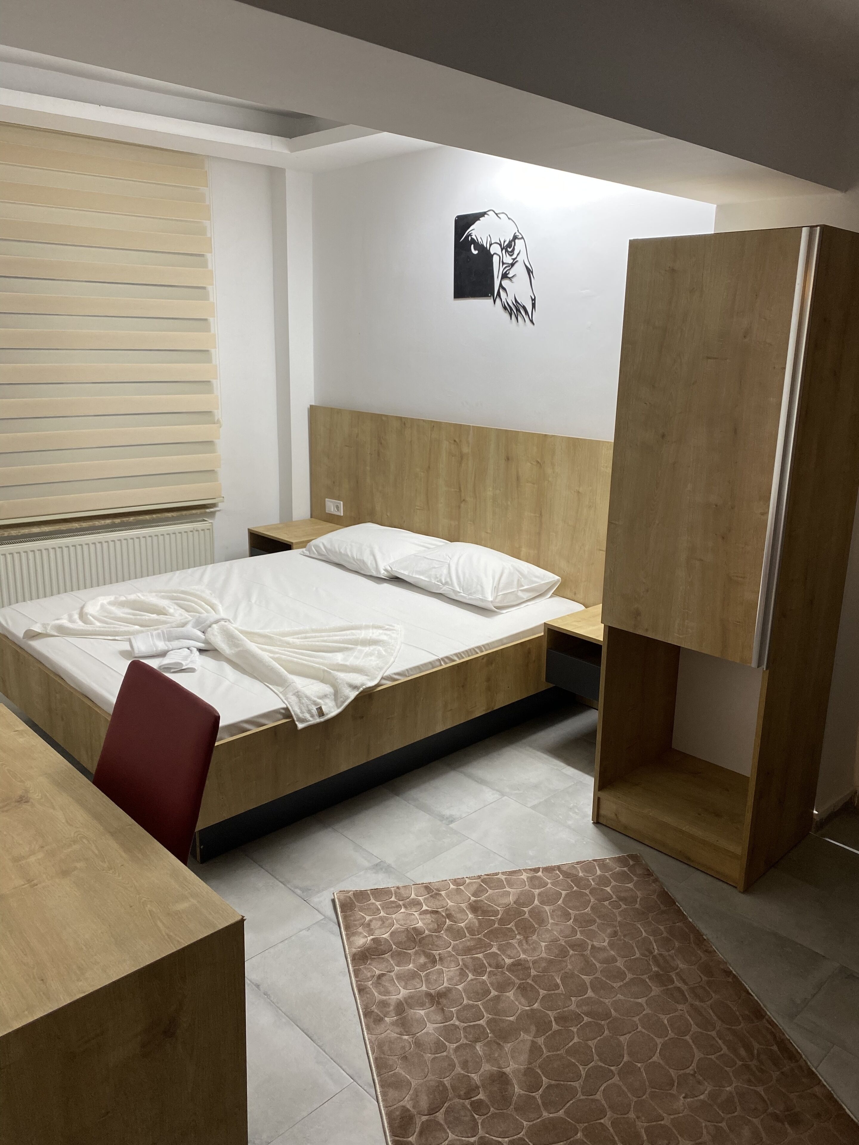 Un dormitorio moderno con estructura de cama de madera, una silla roja, una mesita de noche de madera y un estante fijado a la pared.