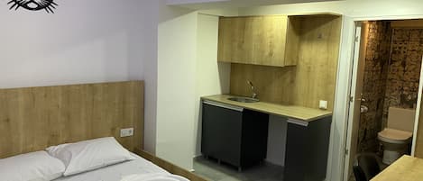 Una habitación pequeña con cama, escritorio con lavabo y retrete.