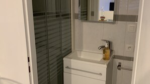 A modern bathroom with a glass shower enclosure, a white sink with a mirror above it, and a toilet with a towel rack.