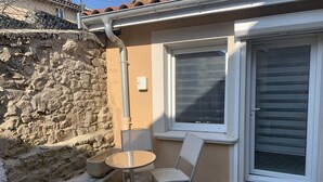 A patio area with a table and chairs, a stone wall, a window with blinds, and a door with a glass panel.