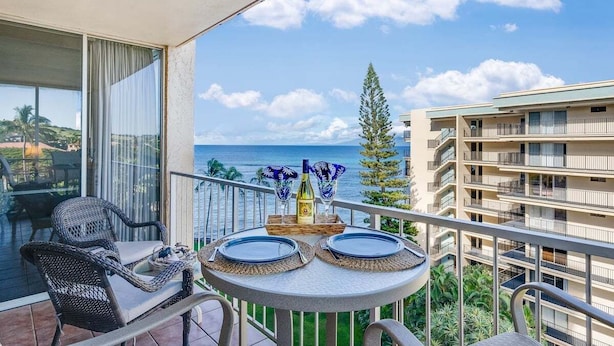 A balcony with a table set for two, overlooking a coastal view. - Spacious OceanFront 2BD w Pool AC-Royal Kahana 701 (Lahaina)