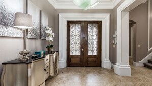Un couloir avec une console de couleur crème, un lampadaire et un grand tableau abstrait accroché au mur.