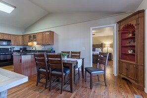 A modern kitchen with wooden cabinets, a dining area with a table and chairs, and a built-in bookshelf.