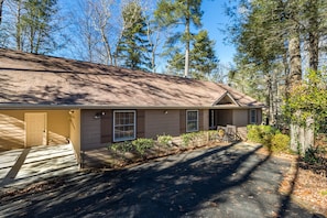A single-story building with a front porch, a garage, and a small front yard with a wooden fence and a few shrubs.