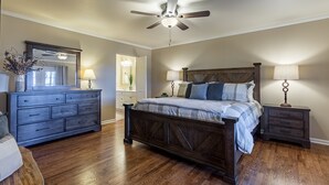 A bedroom with a wooden bed, a dresser, a nightstand, a ceiling fan, and a mirror.