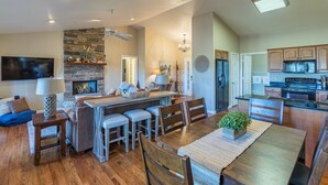 A spacious kitchen with a dining area, wooden cabinets, and a stone fireplace.