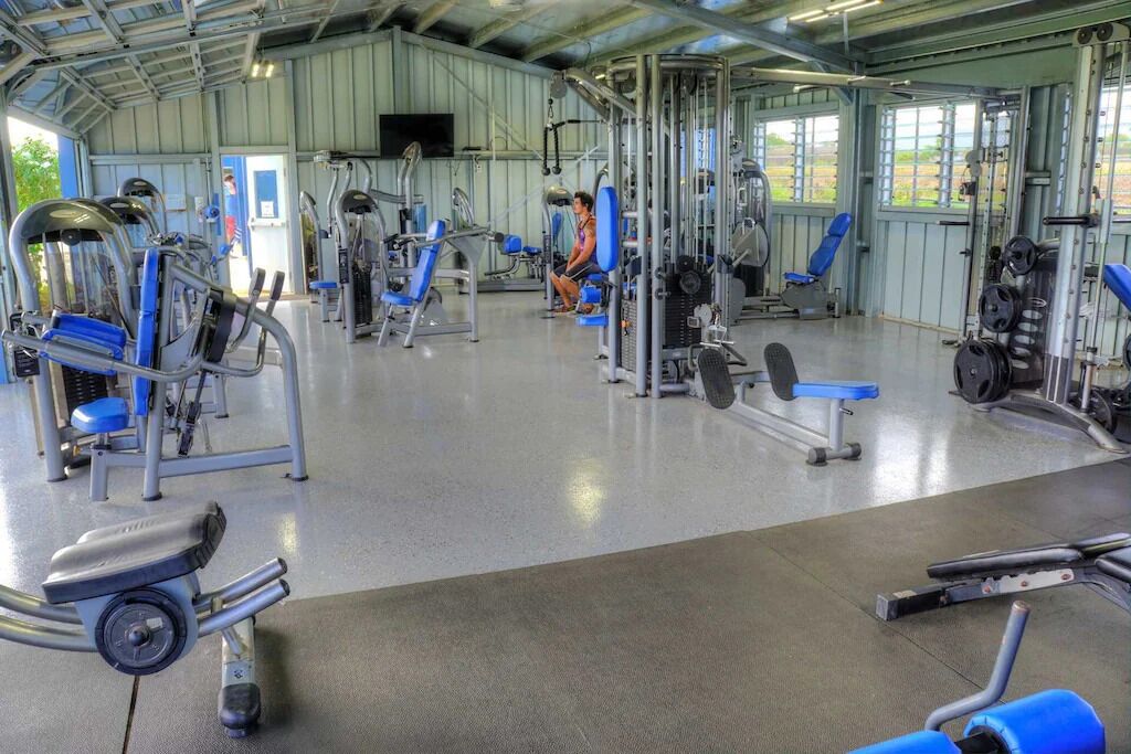 A gym with various exercise machines, a large mirror, and a blue chair.