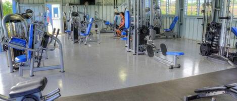 A gym with various exercise machines, a large mirror, and a blue chair.